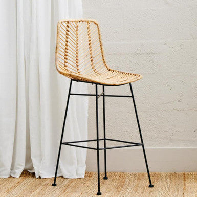 Woven bar stool with black metal legs against a white curtain and light-colored wall.