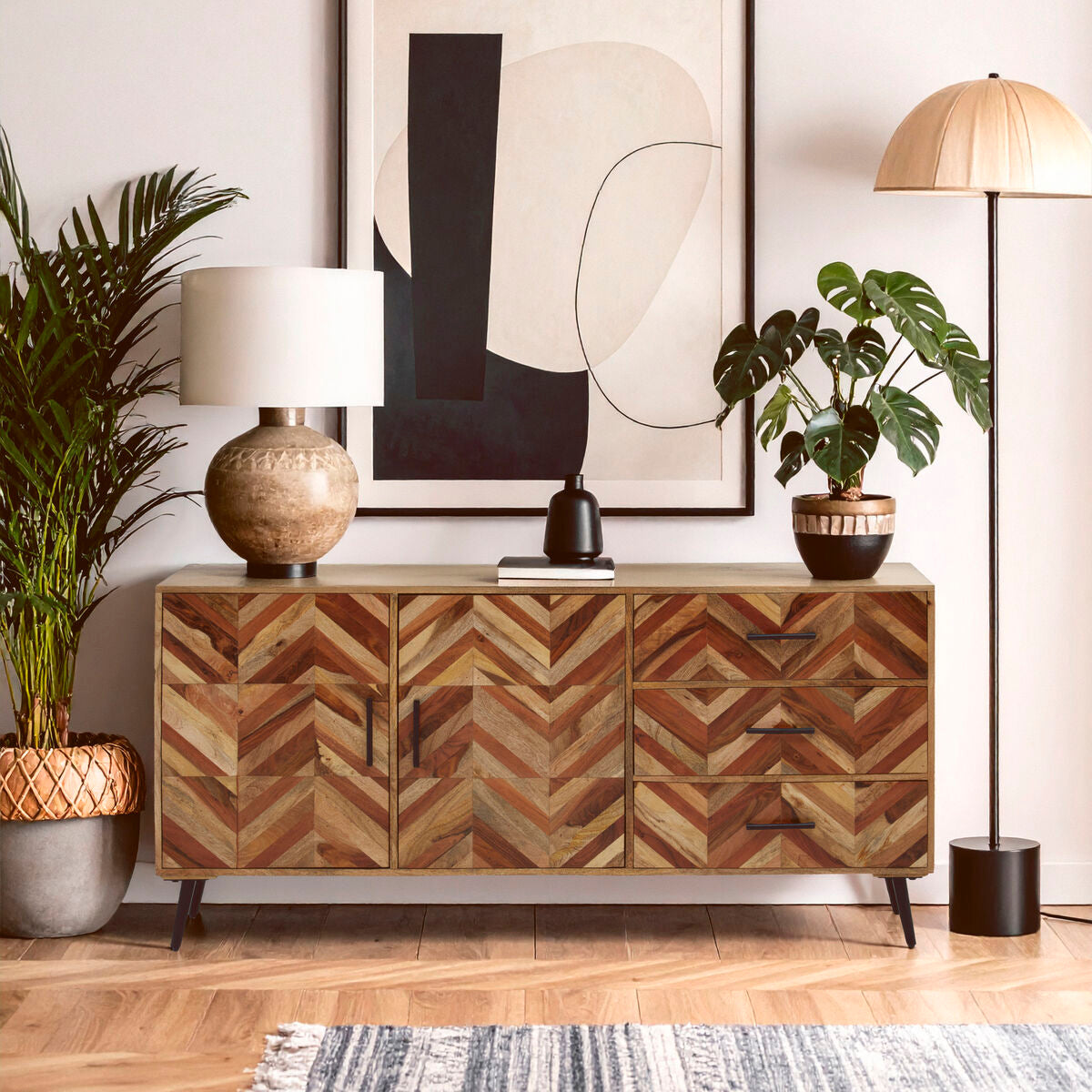 Wooden sideboard with chevron pattern in a room with plants and abstract art.