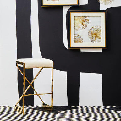 Decorative wall art with gold frames on a black and white abstract wall, accompanied by a gold-framed stool.