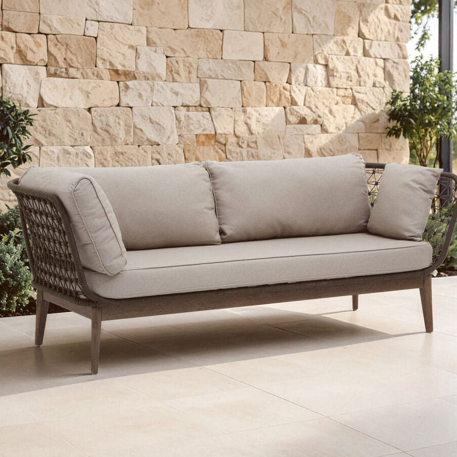 Outdoor sofa with beige cushions against a stone wall.