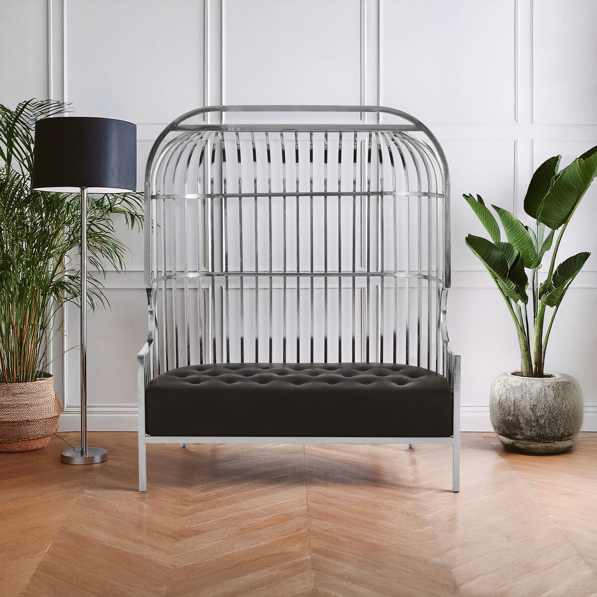 Modern black cushioned chair with metal frame in a room with plants and a lamp.
