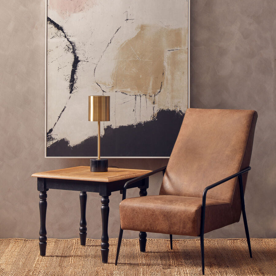 Brown armchair and wooden side table against a gray wall with abstract art