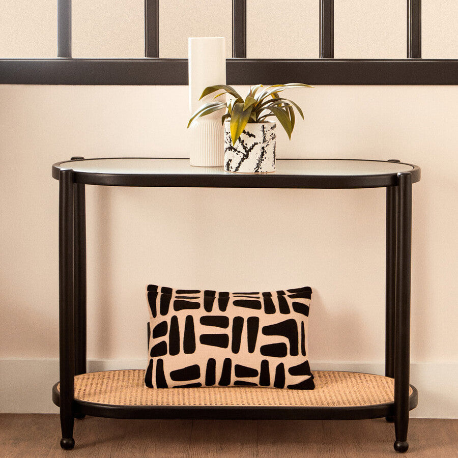 Console table with a decorative pillow and plant against a wall with a geometric pattern.