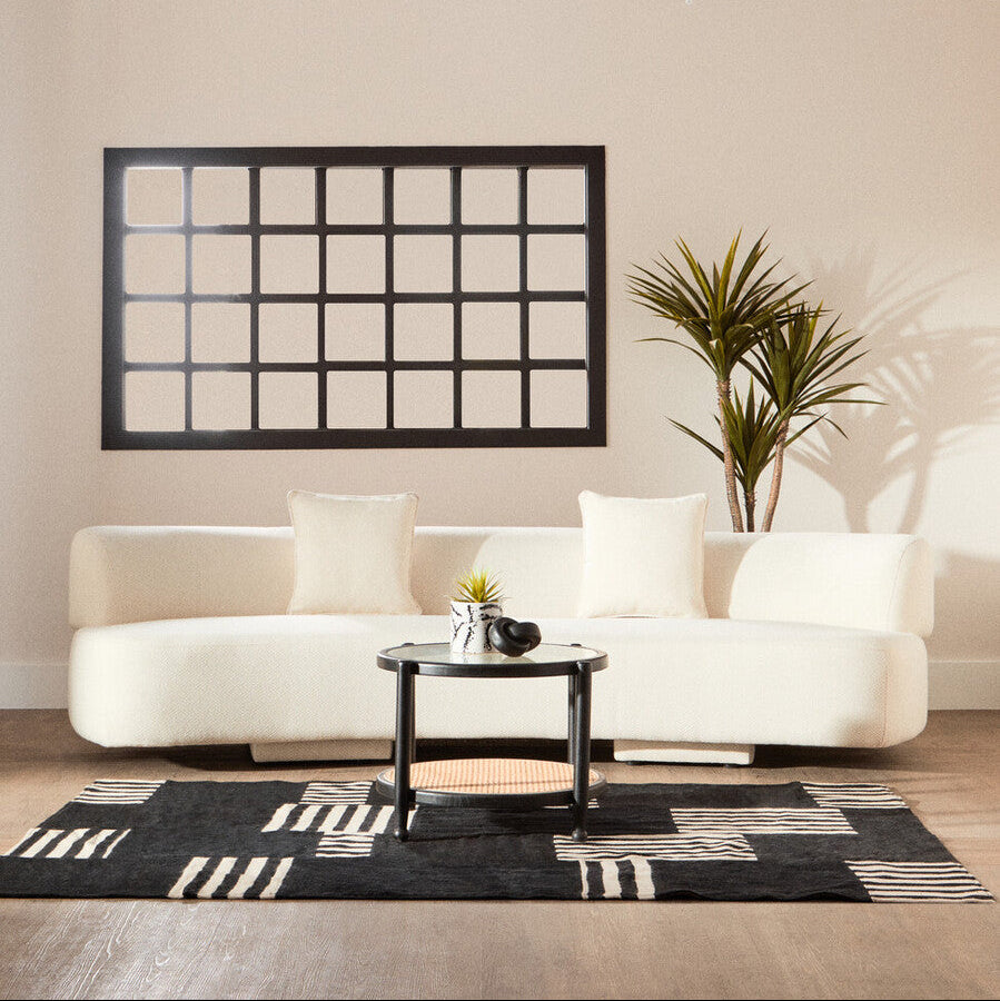 Modern living room with a white sofa, black coffee table, and decorative wall mirror.