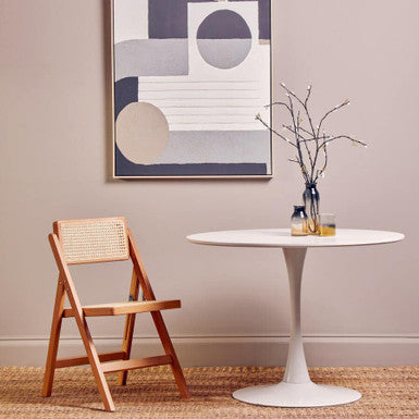 Modern interior with a white round table, wooden chair, and abstract art on the wall.