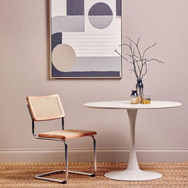 Modern dining room with a white table, wooden chair, and abstract art on the wall.