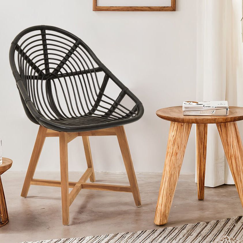 Black woven chair and wooden side table in a room with plants and framed artwork.