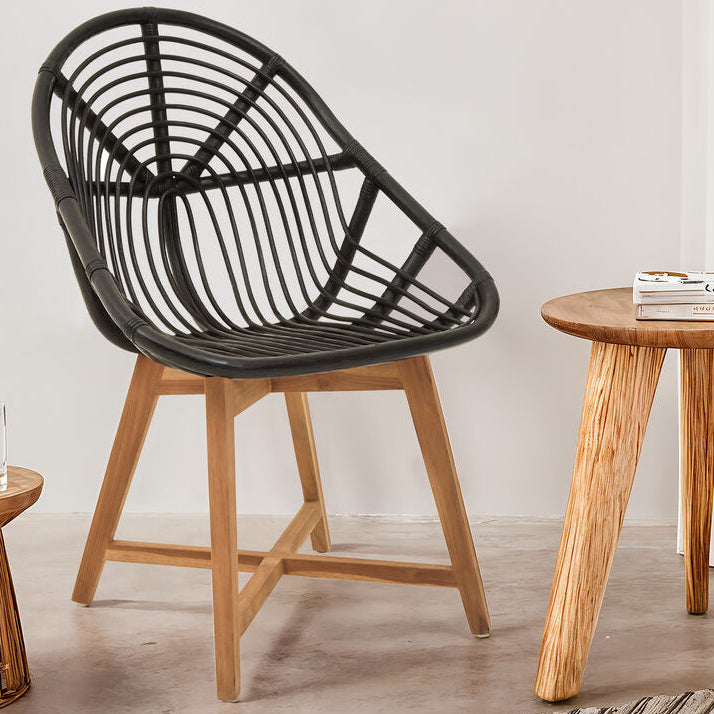 Black woven chair and wooden side table in a room with plants and framed artwork.