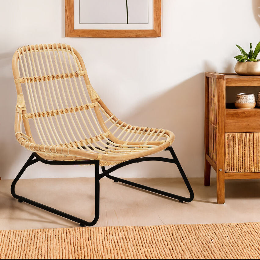 Rattan chair and wooden side table in a room with a plant and wall art.