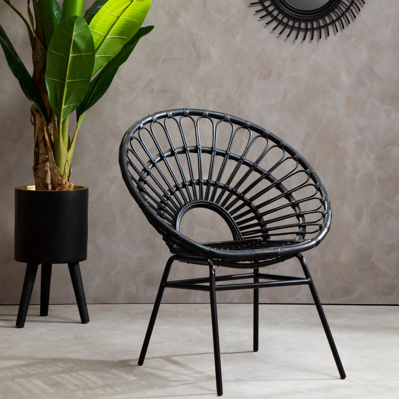 Black wicker chair with a plant and decorative mirror on a gray wall.