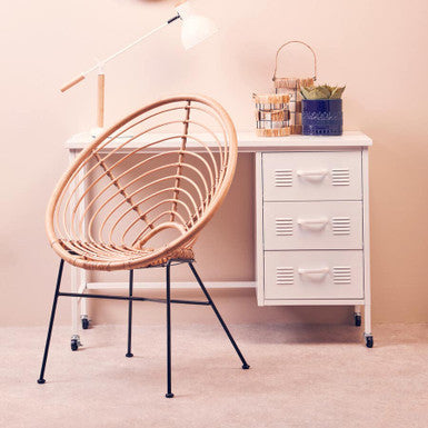 Wicker chair in a room with a white filing cabinet and desk lamp.