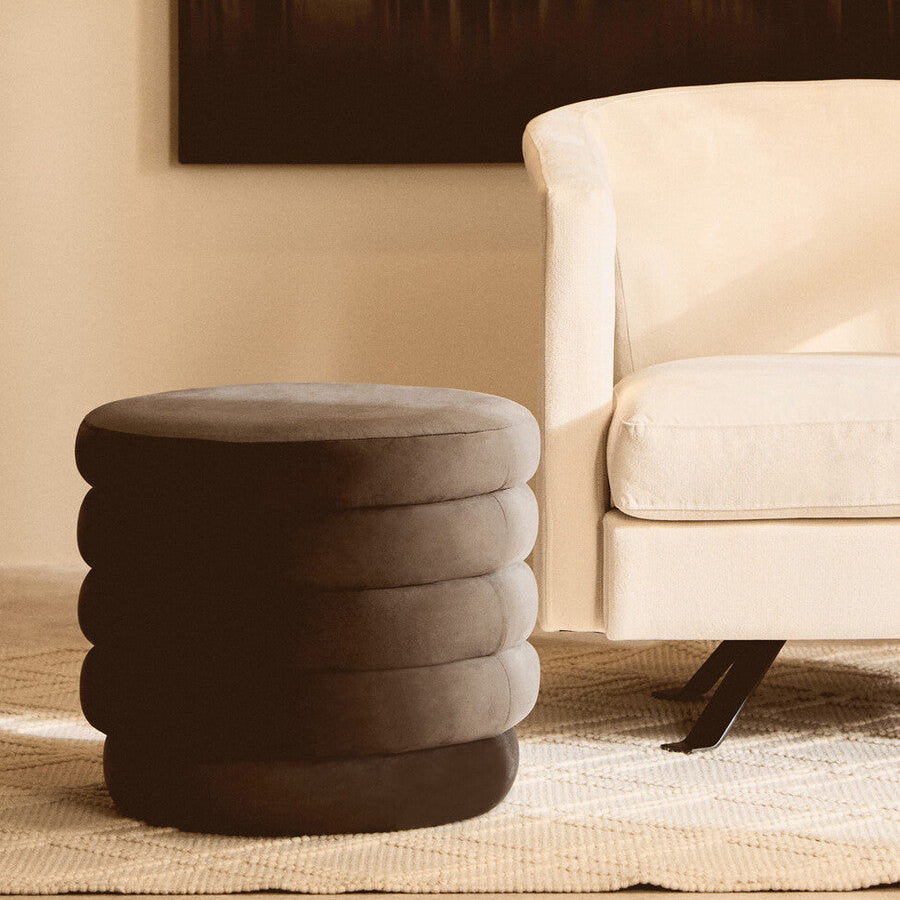 Round, stacked stool in a living room setting with a beige armchair and abstract painting.