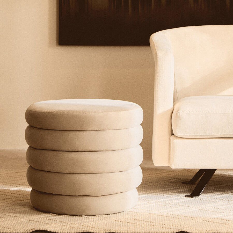 Beige ottoman with stacked circular design next to a beige armchair in a room.