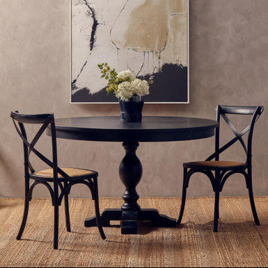 Round dark wooden table with two chairs against a textured wall with abstract art.