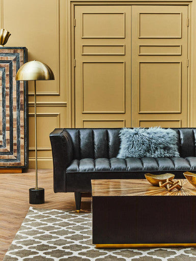 Modern living room with black leather sofa, gold lamp, and wooden coffee table.