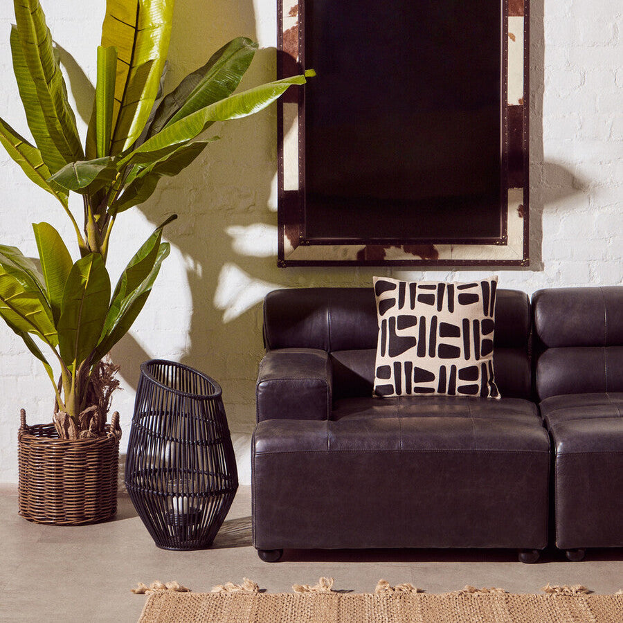 Living room with a brown leather sofa, decorative pillow, plant, and mirror on the wall.
