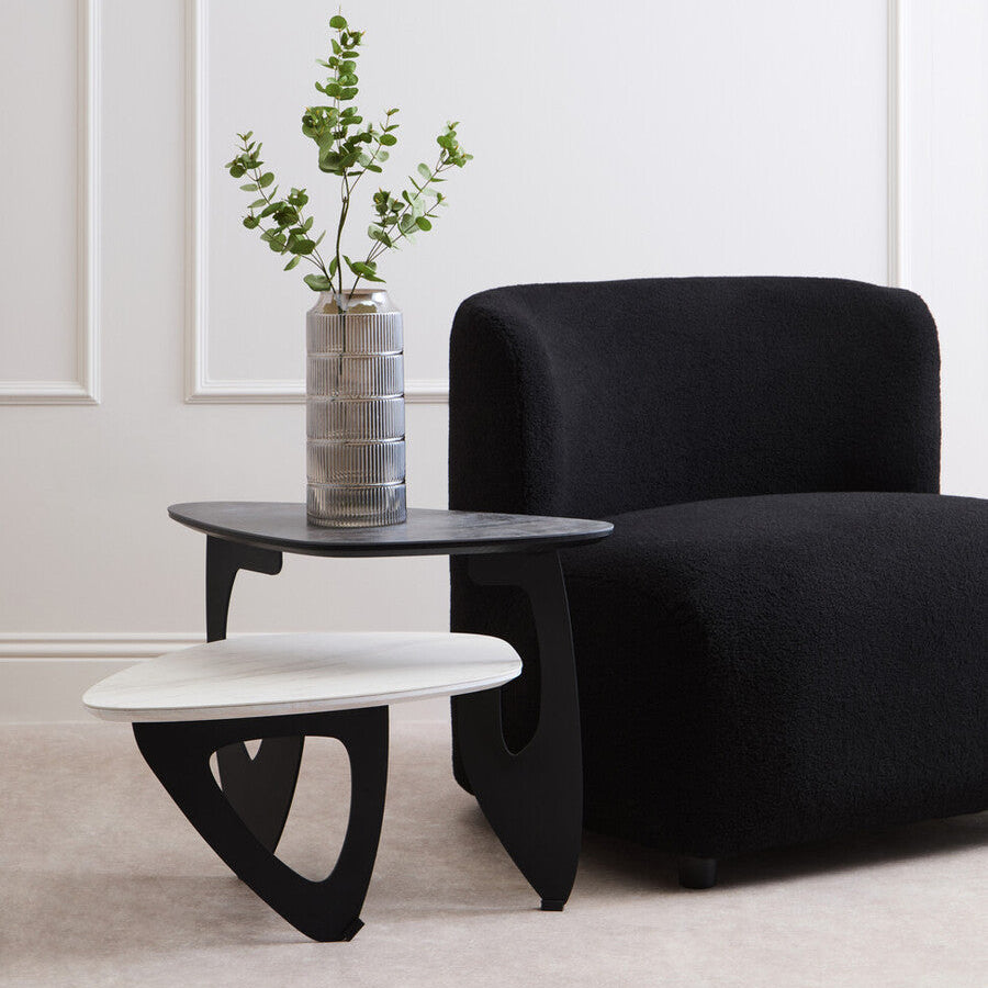 Modern black armchair with a small table and plant in a room with white walls.