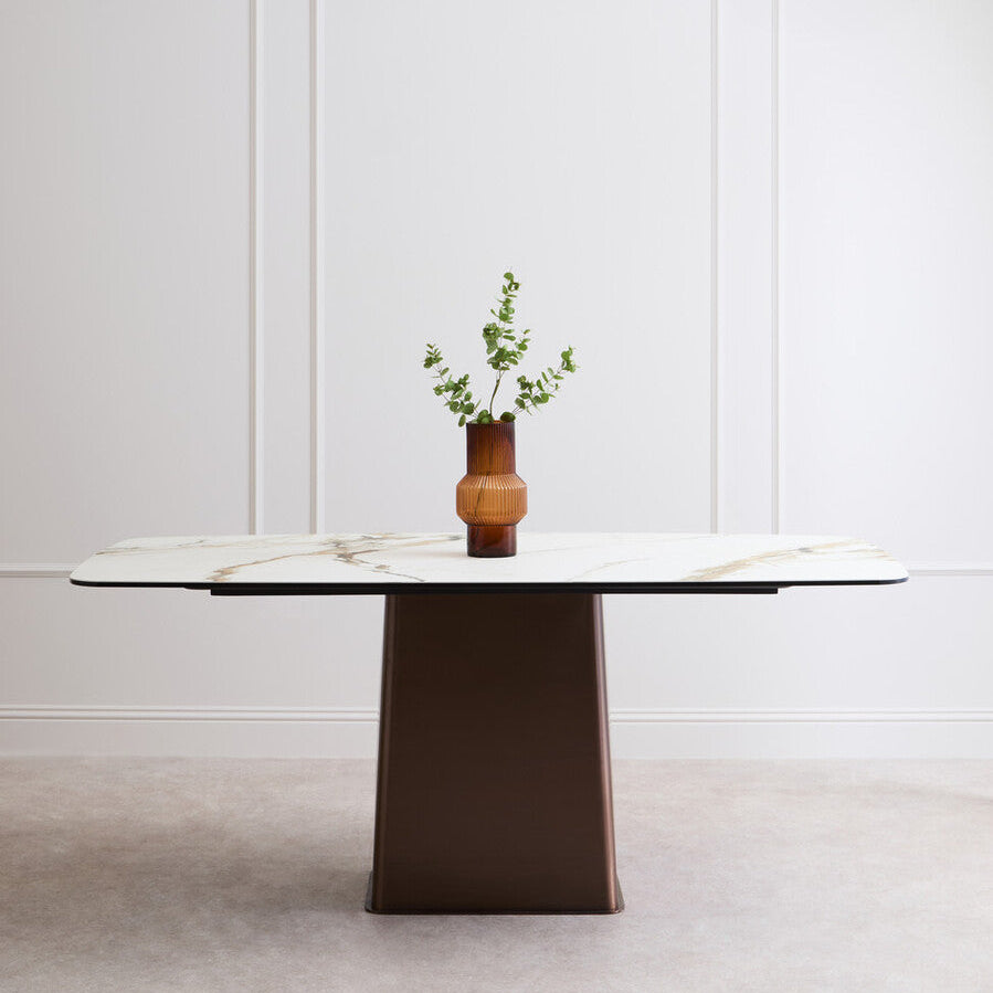 Modern dining table with a vase of greenery against a white wall.