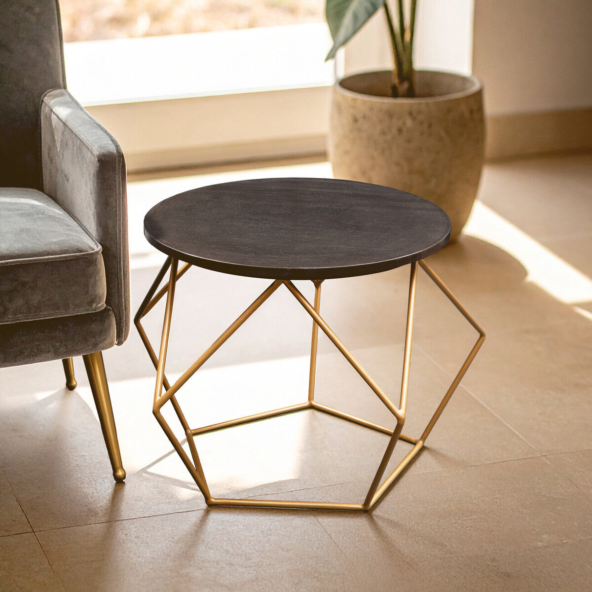 Modern coffee table with geometric gold frame and dark top in a room with a chair and plant.