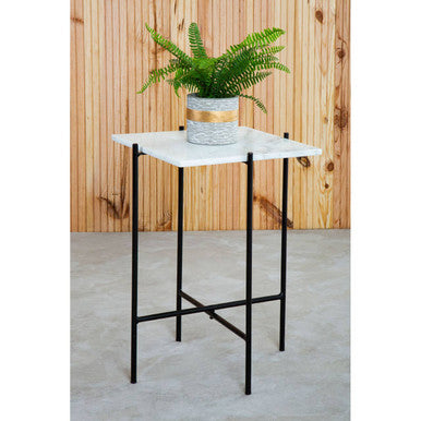 Small square table with marble top and black metal legs against a wooden wall.