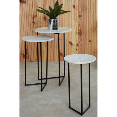 Set of three round side tables with marble tops and black metal legs against a wooden wall.