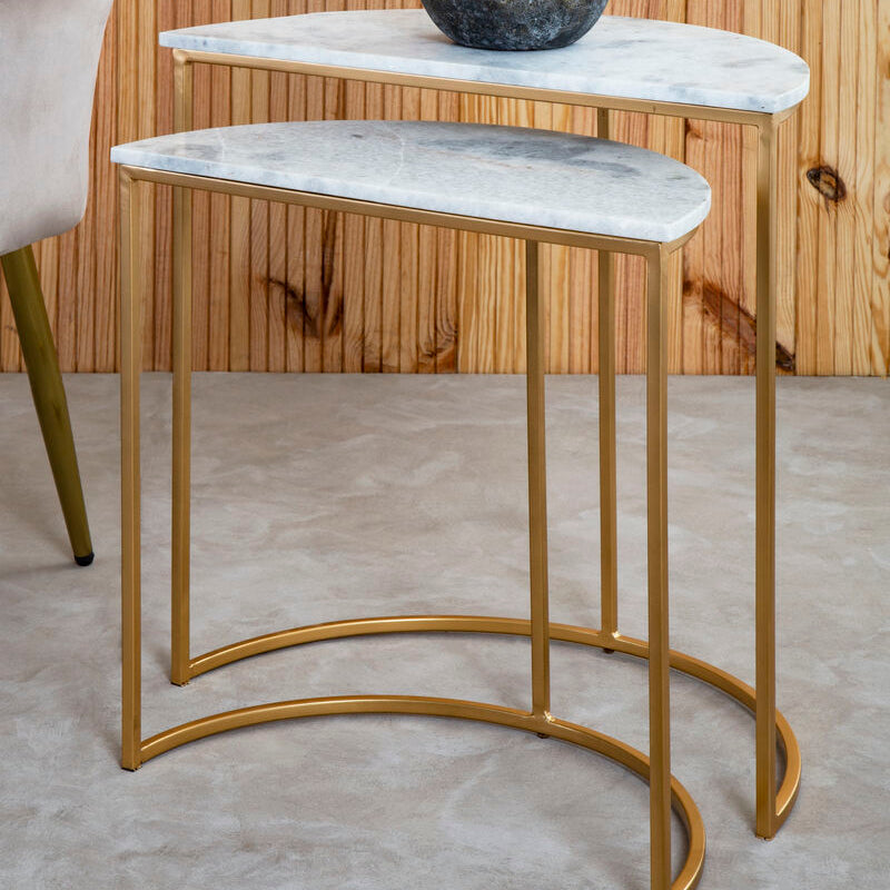 Set of two marble top side tables with gold legs against a wooden wall.