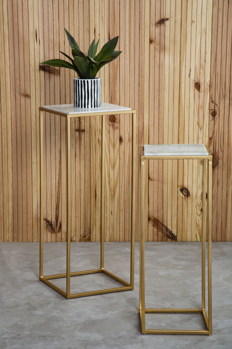 Two gold metal side tables with marble tops against a wooden wall.