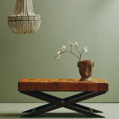 Brown leather bench with a vase of flowers on a green wall