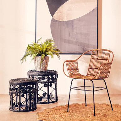 Wicker chair and stools with a plant in a room with abstract art on the wall.