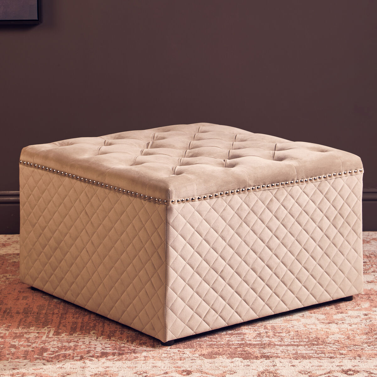 Beige quilted storage ottoman on a textured floor with a dark wall background