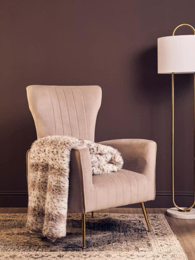 Beige armchair with a fur throw blanket against a dark wall, next to a floor lamp.
