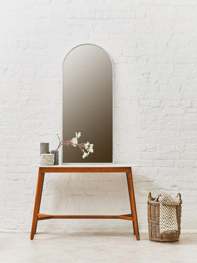 Wooden console table with a tall mirror against a white brick wall.