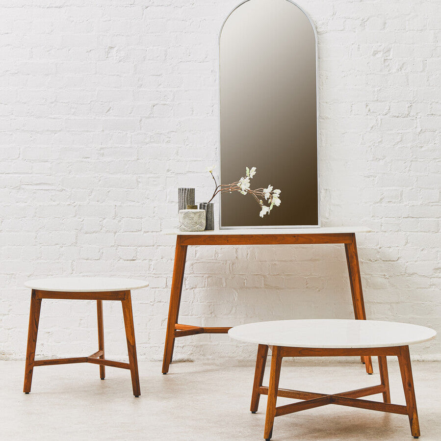 Modern wooden chair and stool with a tall mirror against a white brick wall.