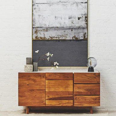 Wooden sideboard with decorative items against a white brick wall with abstract art.