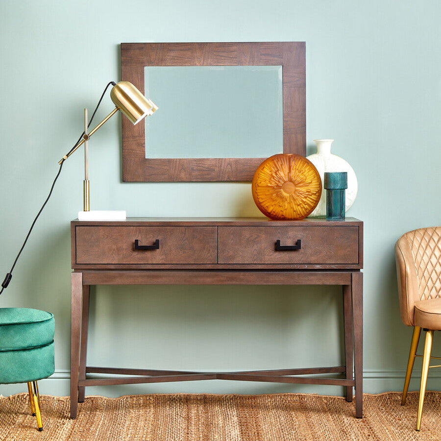 Wooden console table with mirror, lamp, and decorative items against a light green wall.