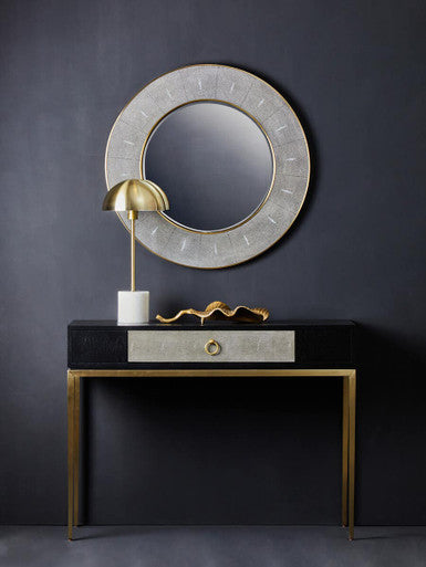 Decorative console table with a round mirror and gold accents against a dark wall.