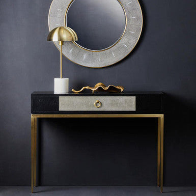 Decorative console table with a round mirror and gold accents against a dark wall.