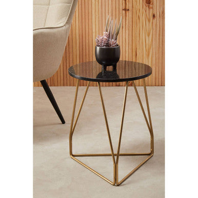 Small round table with black marble top and gold metal legs in a room setting.