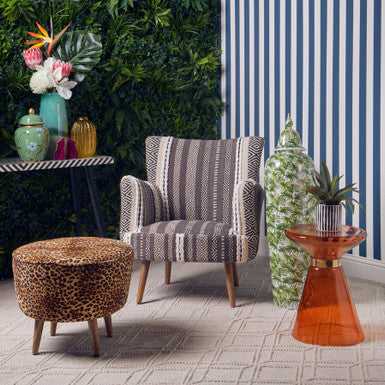 Modern interior with a striped armchair, leopard print ottoman, and orange side table against a green wall.