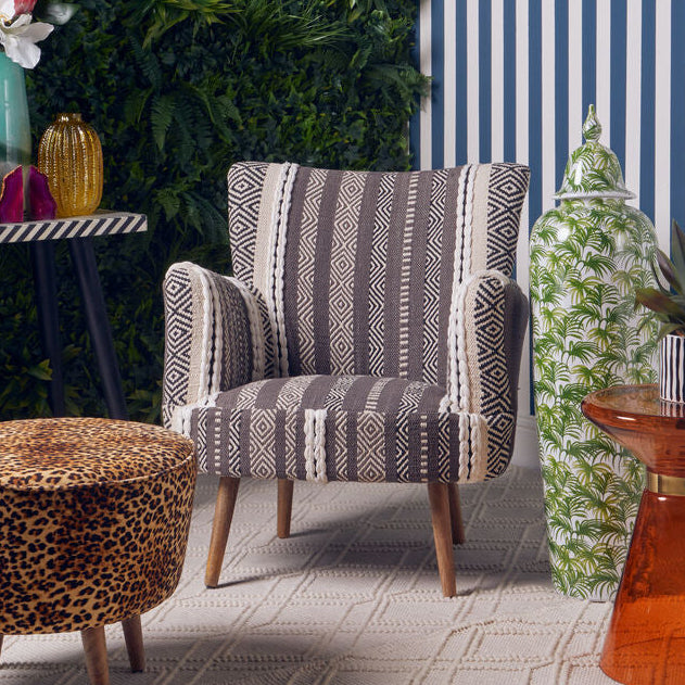 Modern interior with a patterned armchair, leopard print ottoman, and orange table against a striped wall.