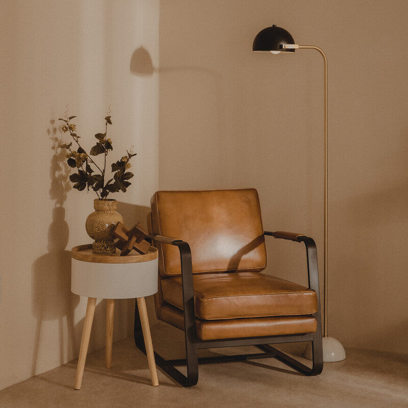 Brown leather armchair with a small table and floor lamp against a beige wall.