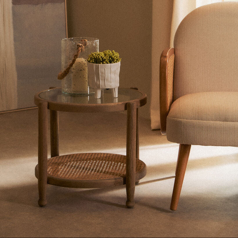 Wooden side table with decorative items next to a beige armchair in a softly lit room.
