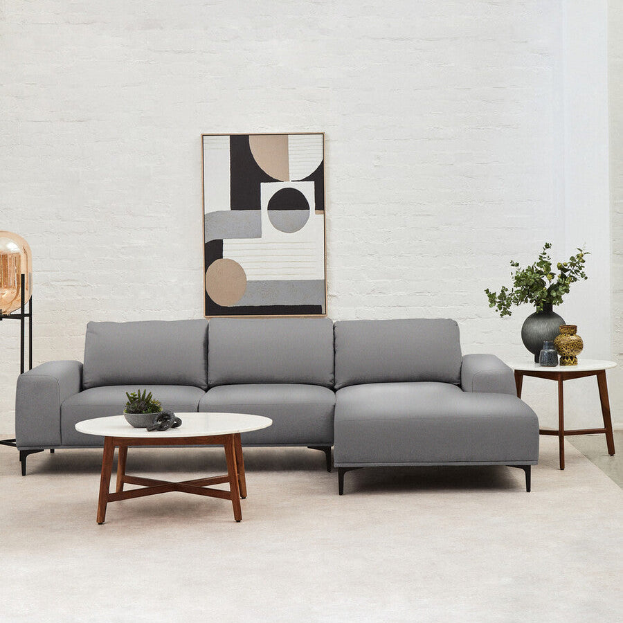 Modern living room with a gray sectional sofa, round wooden coffee table, and abstract art on the wall.
