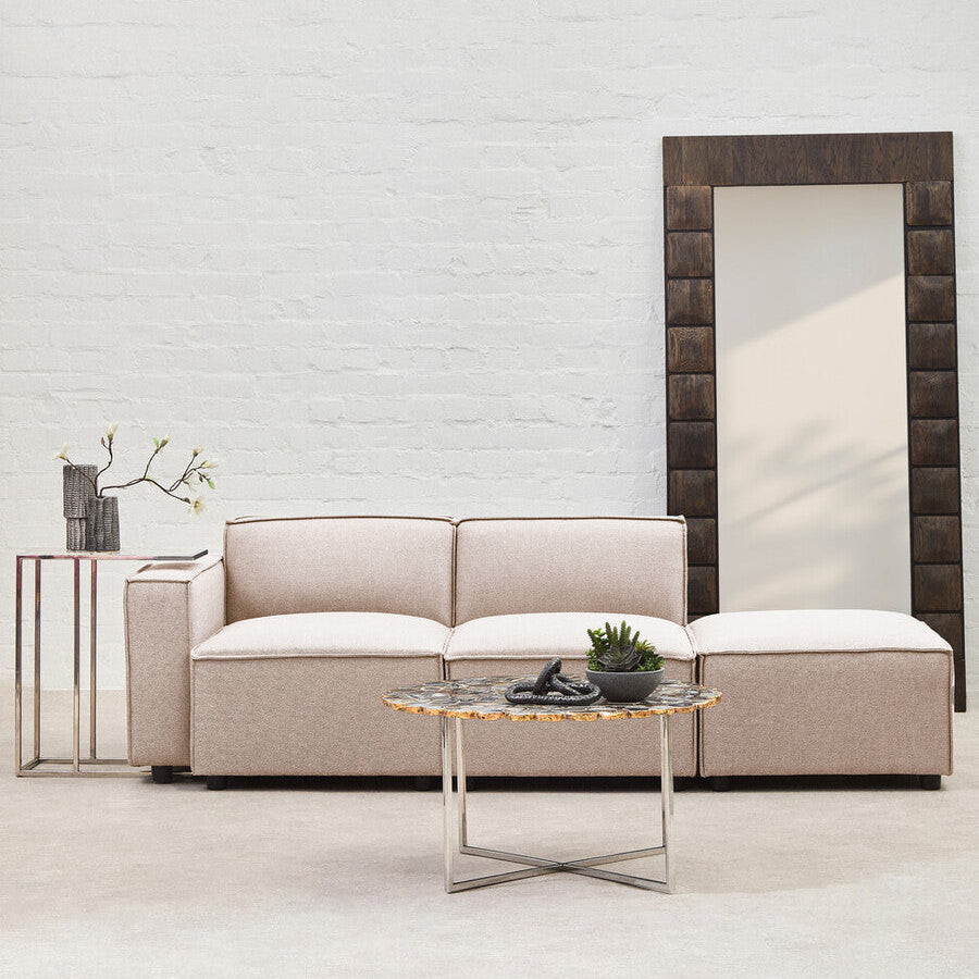 Modern living room with a beige sofa, coffee table, and large mirror against a white brick wall.