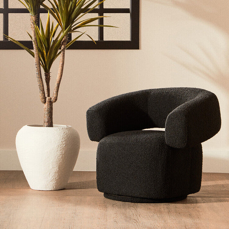 Modern black armchair next to a potted plant on a wooden floor with a neutral wall background