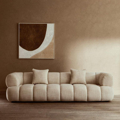 Beige sofa in a room with a brown wall and abstract art