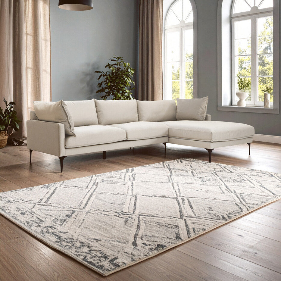 Modern living room with a beige sectional sofa, patterned rug, and large windows.