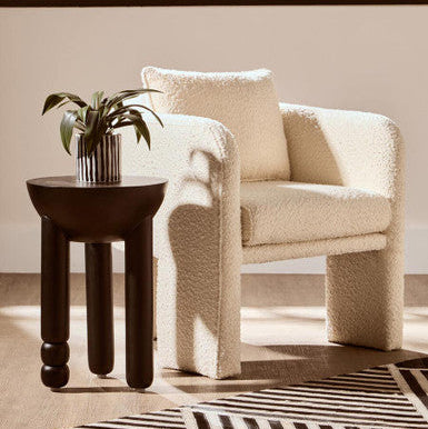 Beige armchair with a small round table and plant in a room with a striped rug.