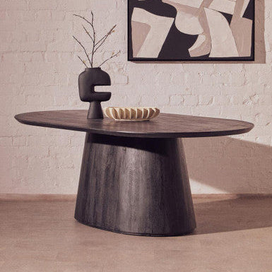 Wooden dining table with decorative items against a light brick wall with abstract art.