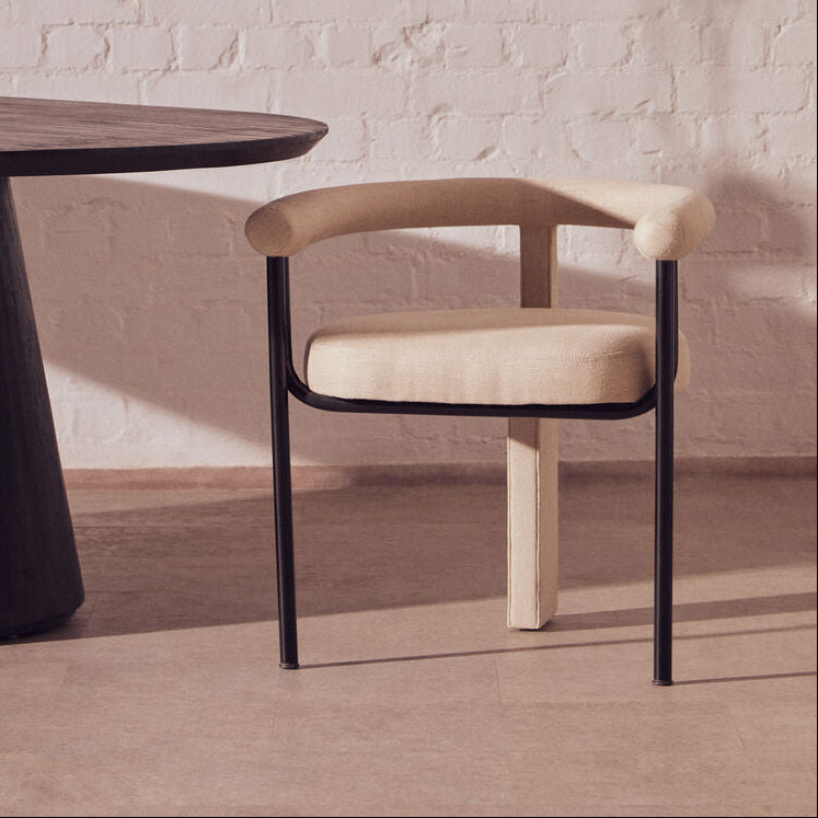 Modern chair with beige cushion and black frame next to a round wooden table in a room with abstract art on the wall.